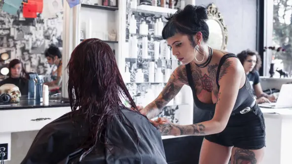 junge Frau mit vielen Tattoos am Körper schneidet in einem Friseursalon einer Kundin die Haare