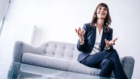Frau sitzt auf grauem Sofa und spricht