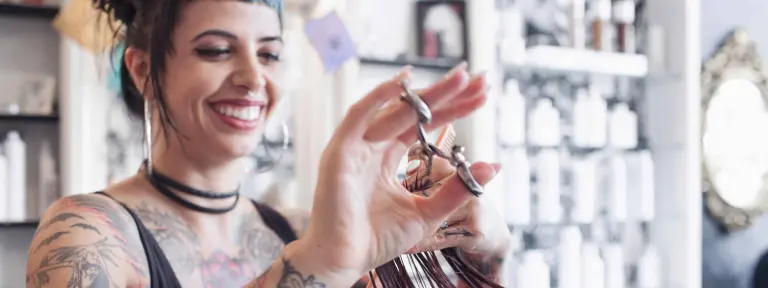Junge Frau mit vielen Tattoos am gesamten Körper arbeitet in einem Friseursalon und schneidet einer Kundin die Haare
