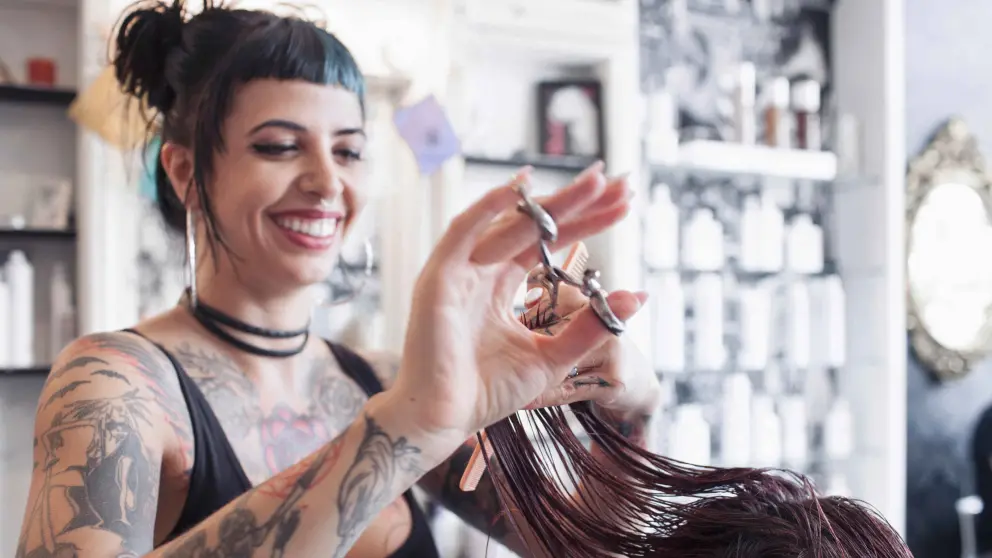 Junge Frau mit vielen Tattoos am gesamten Körper arbeitet in einem Friseursalon und schneidet einer Kundin die Haare