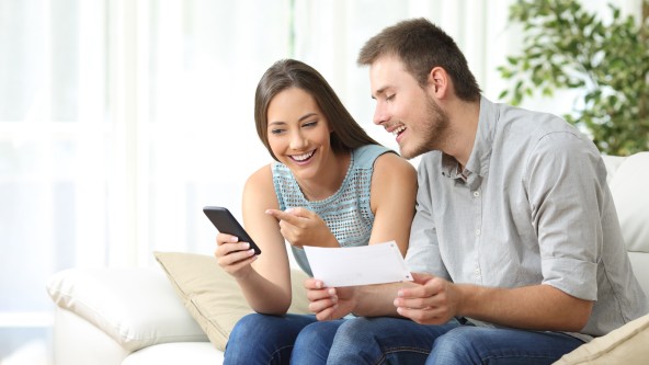 Mann und Frau sitzen auf Sofa und schauen in ein Smartphone