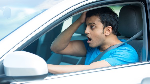 Mann hält sich mit offenen Mund den Kopf auf Fahrersitz eines Autos