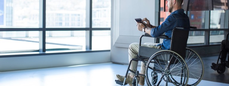 Mann sitzt im Rollstuhl und hält Tablet in der Hand