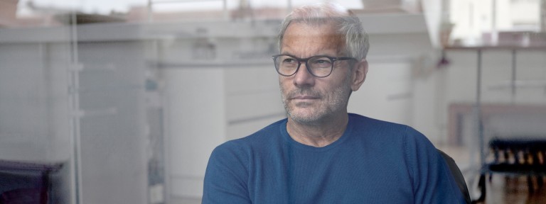 Älterer Mann mit grauen Haaren und Brille sitzt vor einer Fensterscheibe