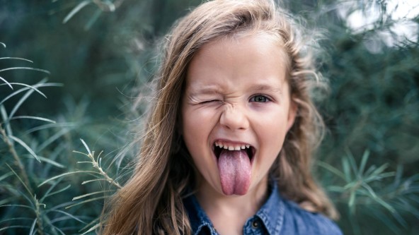 Junges Mädchen streckt Zunge aus dem Mund drückt ein Auge zu