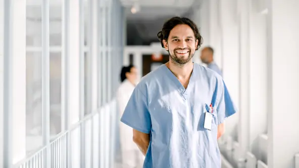 Krankenpfleger im blauen Oberteil lacht in die Kamera