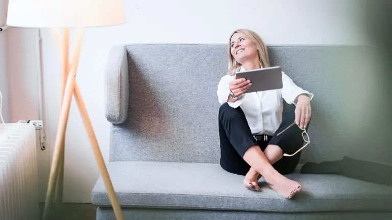 Frau sitzt lächelnd auf der Couch und hält ein Tablet in der Hand