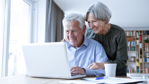 Älteres Ehepaar blickt lachend in deinen aufgeklappten Laptop