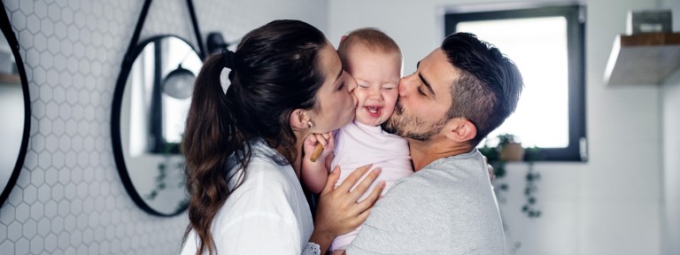 Frau und Mann küssen ihr Kleinkind