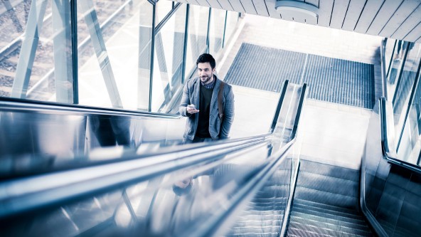 Mann mit Handy in der Hand fährt lange Rolltreppe nach oben
