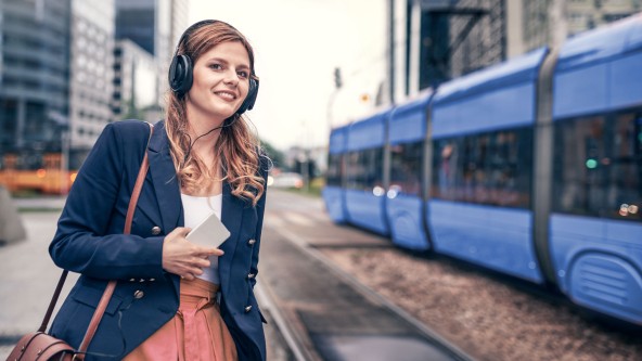 Frau mit Kopfhörer über ihre Ohren steht am Bahnhof