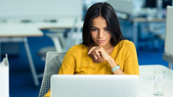 Junge dunkelhaarige Frau in gelbem Pullover sitzt vor Laptop