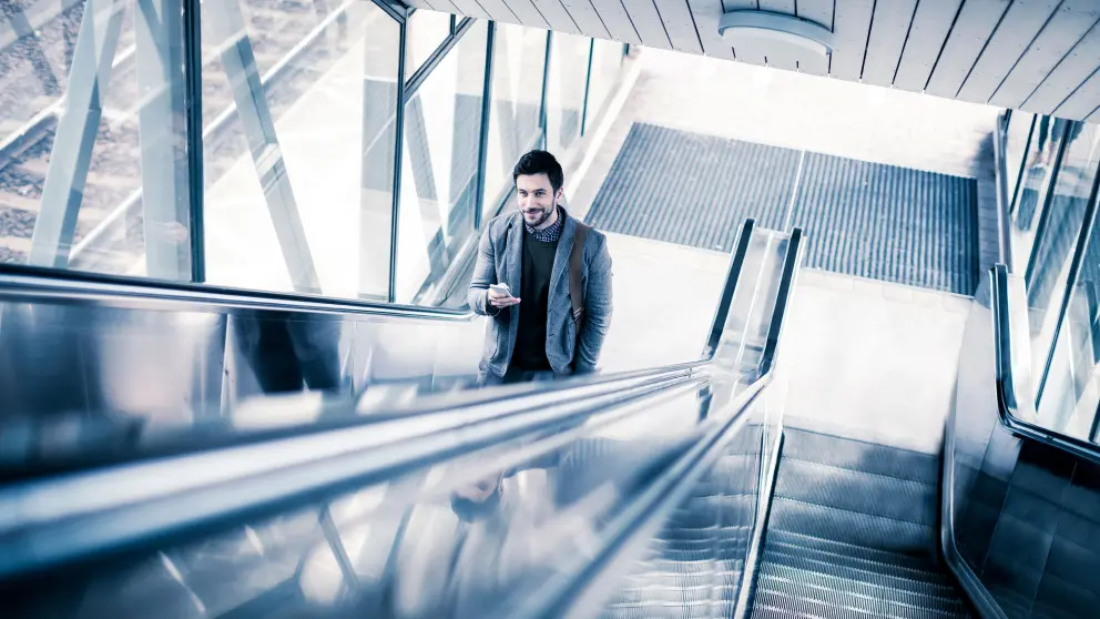 Mann mit Handy in der Hand fährt lange Rolltreppe nach oben