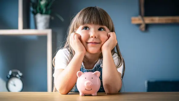 kleines Mädchen hält den Kopf in den Händen und hat vor sich ein rosa Sparschwein stehen