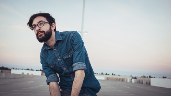 Junger brunetter Mann mit Bart und Brille sitzt auf Parkdeck unter Laterne