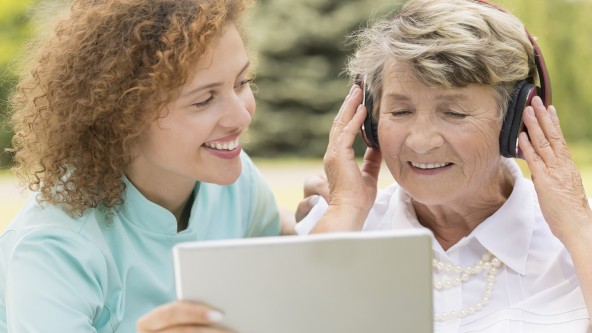Junge Frau mit Tablet, ältere Frau mit Kopfhörer steht daneben