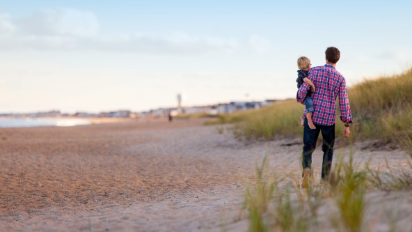 Mann steht mit kleinem Kind auf dem Arm am Strand
