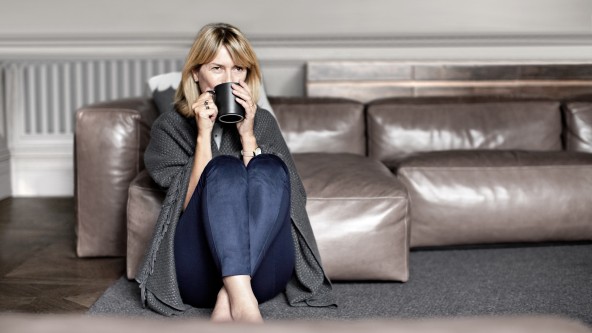 Frau sitzt mit Decke am Boden und trinkt aus einer Kaffeetasse