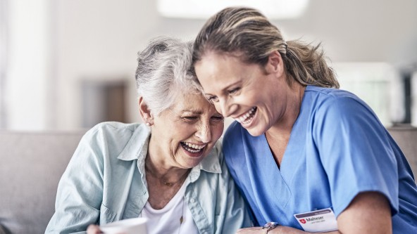 Pflegerin lacht neben und mit einer älteren Frau