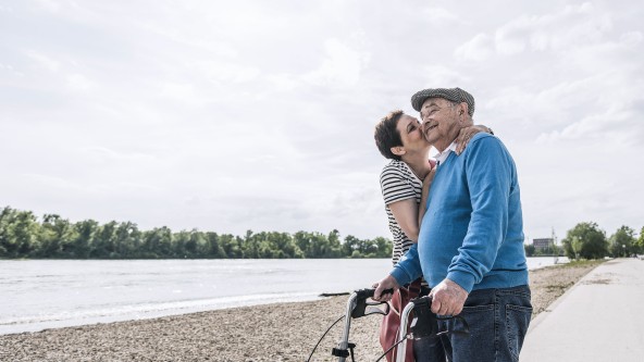 Älteres Paar steht neben einem großen Fluss und der Mann wird von der Frau auf die Wange geküsst