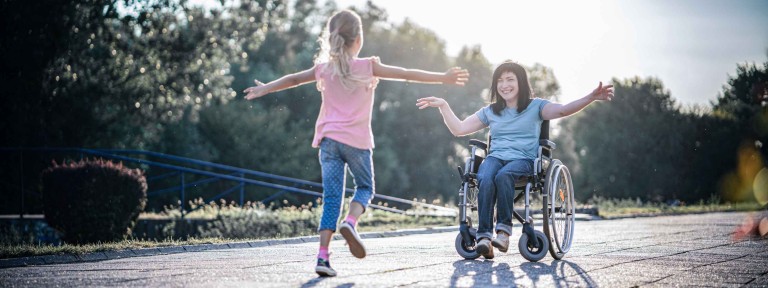 Mädchen läuft mit offenen Armen einer Frau im Rollstuhl entgegen