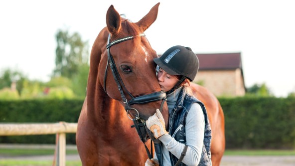 Junge Reiterin küsst Pferd auf die Stirn