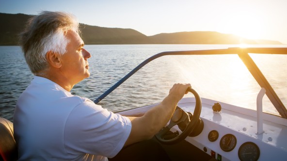 Älterer Mann fährt in einem Boot dem Sonnenuntergang entgegen