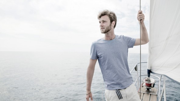 Mann steht im T-Shirt auf einem Segelboot