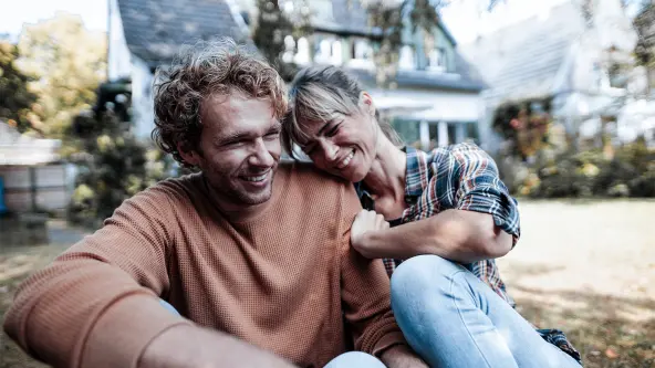 Lächelndes Paar sitzt im Garten vor ihrem Haus