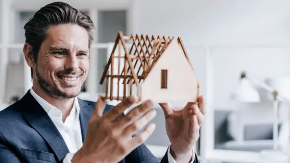 Lächelnder Mann hält ein Hausmodell aus Holz