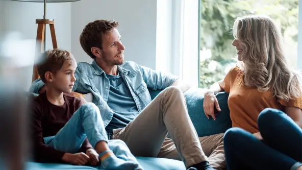 Vater und Mutter sitzen gemeinsam mit ihrem Kind auf dem Sofa