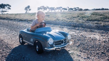 Blonder Junge sitzt in fahrendem kleinen Kinder-Auto