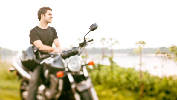 Junger Mann steht mit seinem Motorrad an einem See