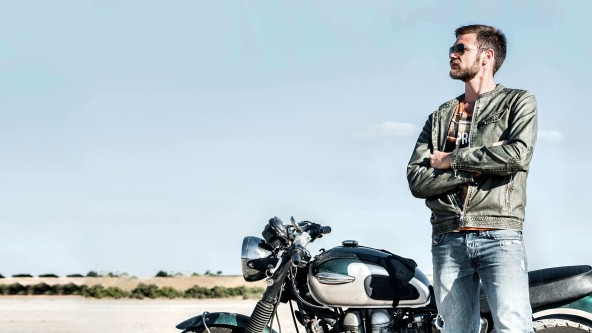 Mann mit Sonnenbrille steht neben seinem geparkten Motorrad