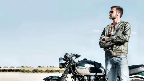Mann mit Sonnenbrille steht neben seinem geparkten Motorrad