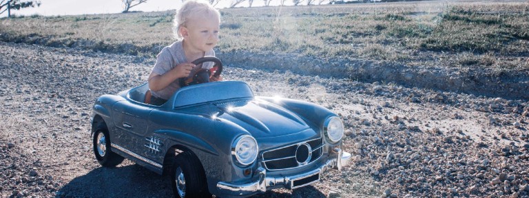 Blonder Junge sitzt in fahrendem kleinen Kinder-Auto