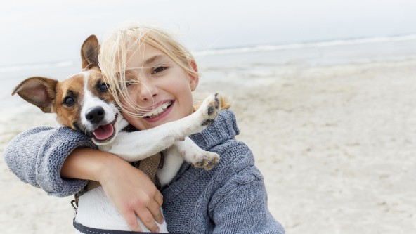 Blondes Mädchen macht Selfie mit Hund an einem Strand