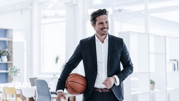 Lächelnder Mann im Anzug mit einem Basketball unter dem Arm