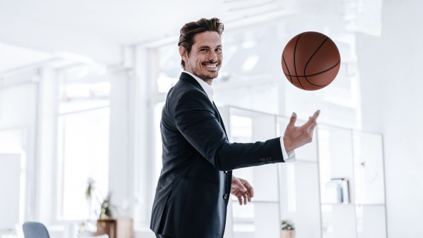 Lächelnder Mann im Anzug spielt mit einem Basketball