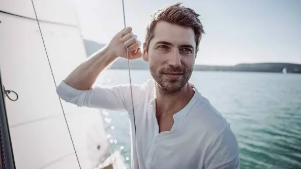 Junger Mann hält sich an Seil auf einem Boot fest