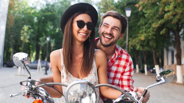 Junges Paar sitzen lachend auf einem Motorroller
