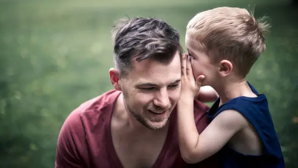 Ein Junge flüstert seinem Vater etwas in Ohr