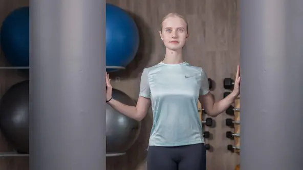 Eine junge Sportlerin steht zwischen 2 Säulen und drückt mit ihren Händen gegen beide Säulen