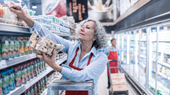 Ältere Frau räumt ein Regal im Supermarkt ein