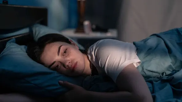 Eine junge Frau liegt nachts wach im Bett