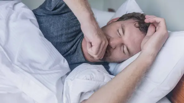 Mann liegt erschöpft im Bett und hustet