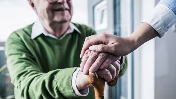 Frau legt ihre Hand auf beide Hände eines älteren Mannes mit grünem Pullover