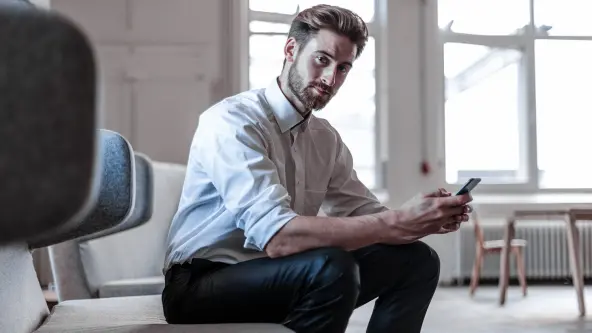 Mann im Hemd sitzt auf Stuhl und hat Smartphone in der Hand