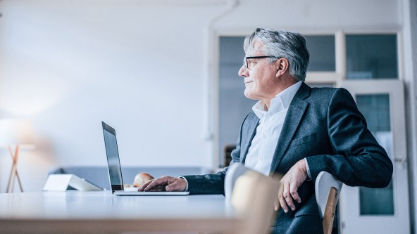 Älterer Herr mit Brille sitzt vor Laptop
