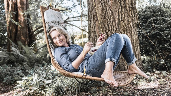 Frau mittleren Alters liegt in einem Hängestuhl an einem Baum